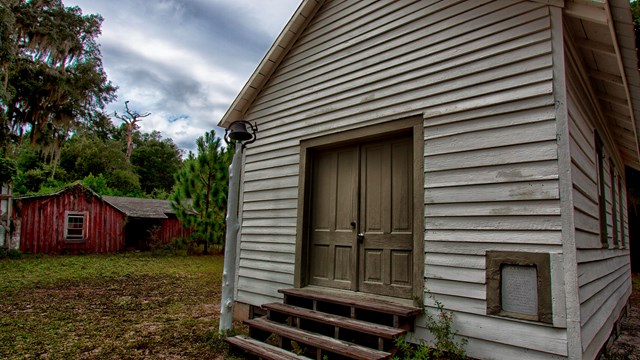 One room white church with a red rundown house in the back